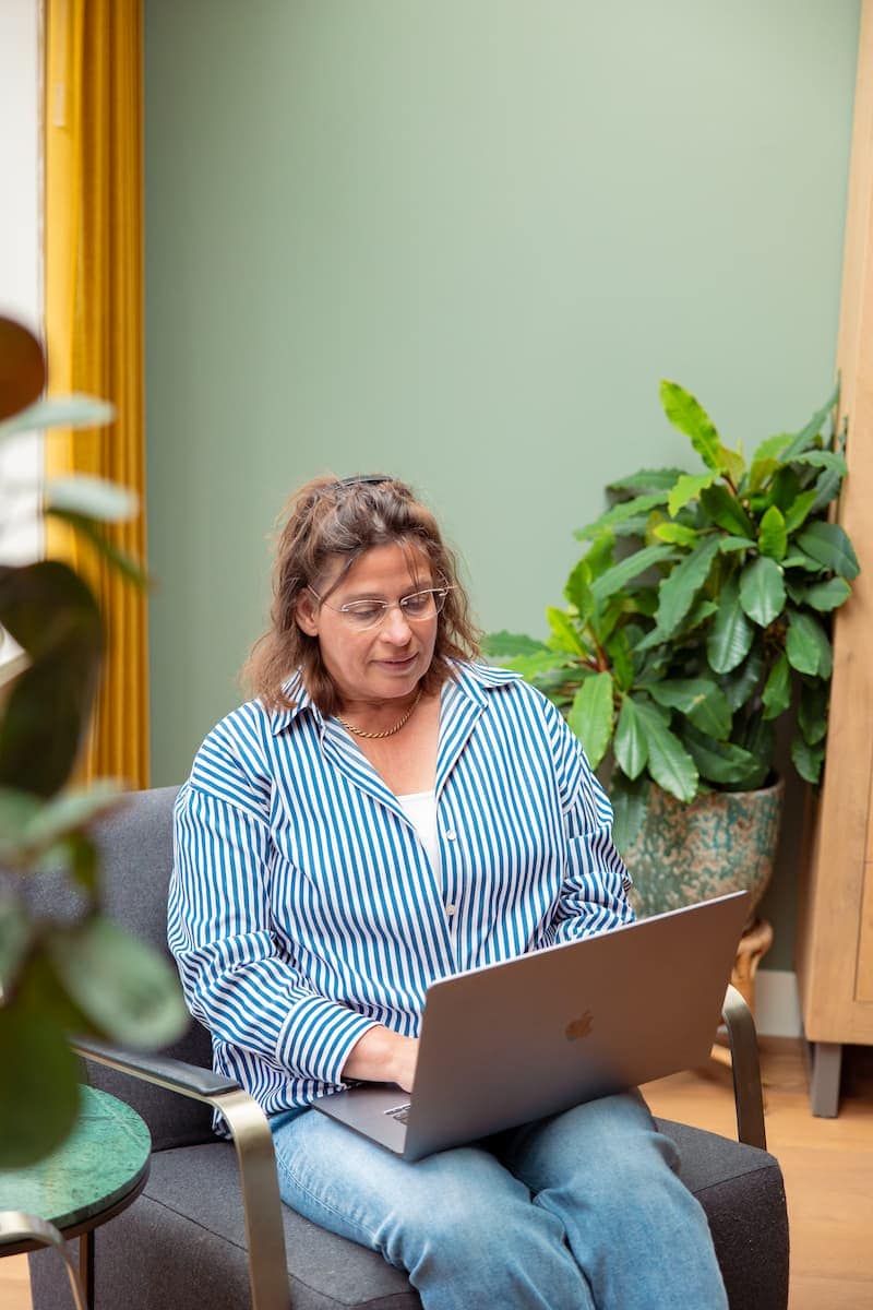 Vrouw werkt op laptop in zithoek met groene muur en kamerplanten