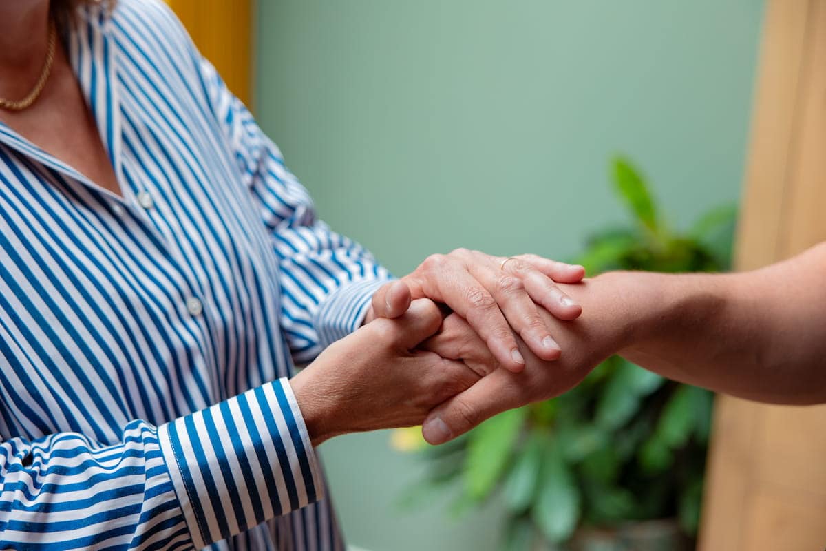 Handen die elkaar vasthouden als troostend en ondersteunend gebaar, Samen Minder Zorgen