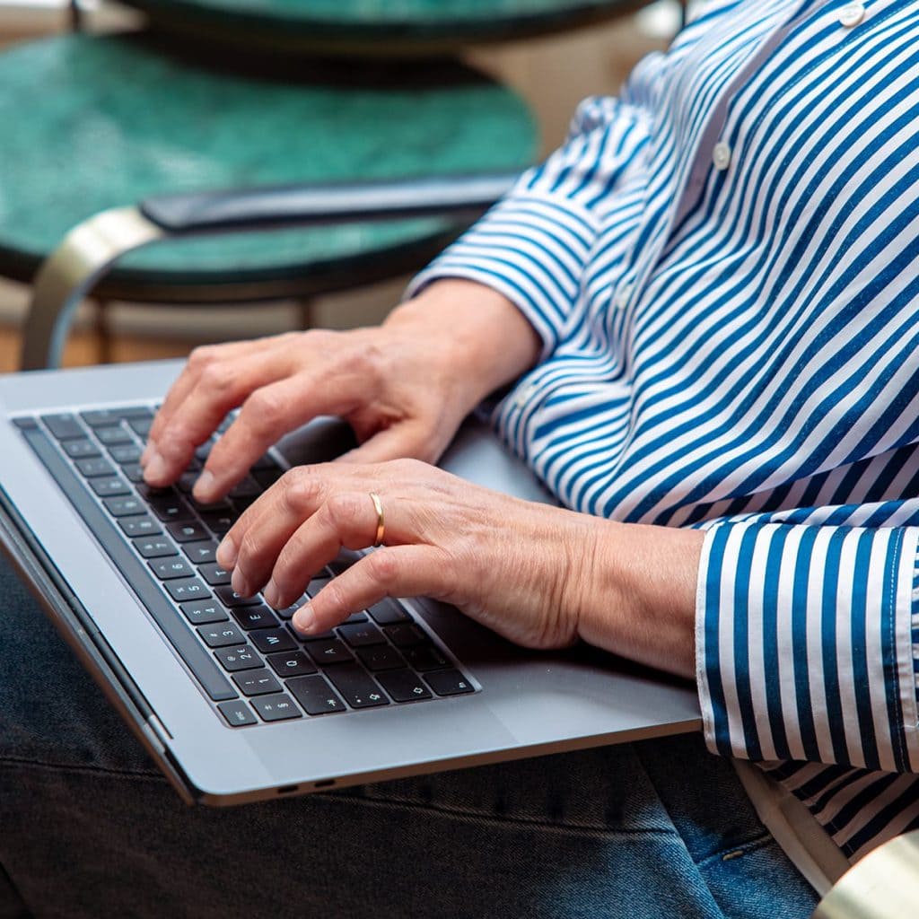 Handen die op het toetsenbord van een laptop typen, met gestreept overhemd en gouden ring
