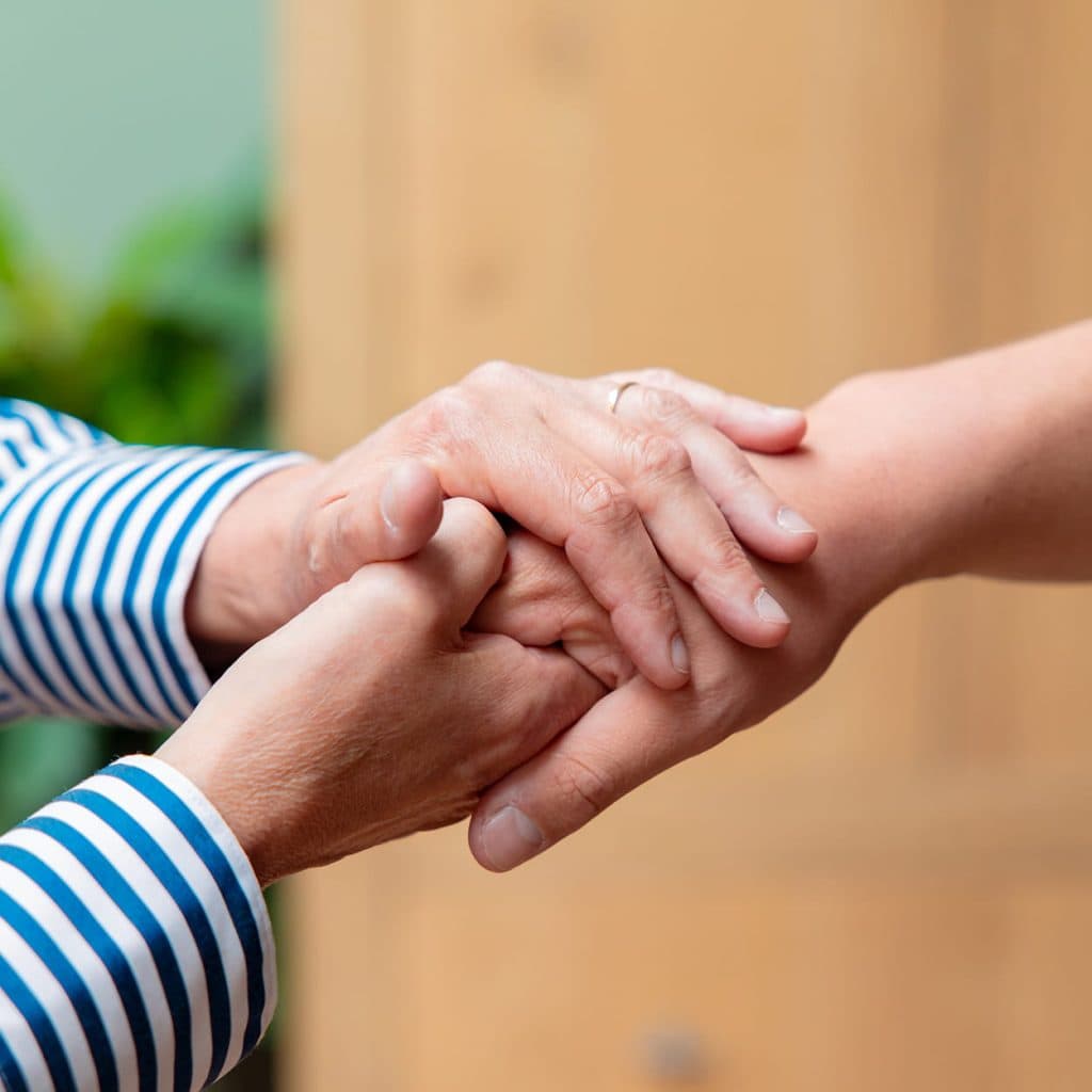 Twee handen die elkaar vasthouden in een steunende, zorgzame houding - Samen Minder Zorgen